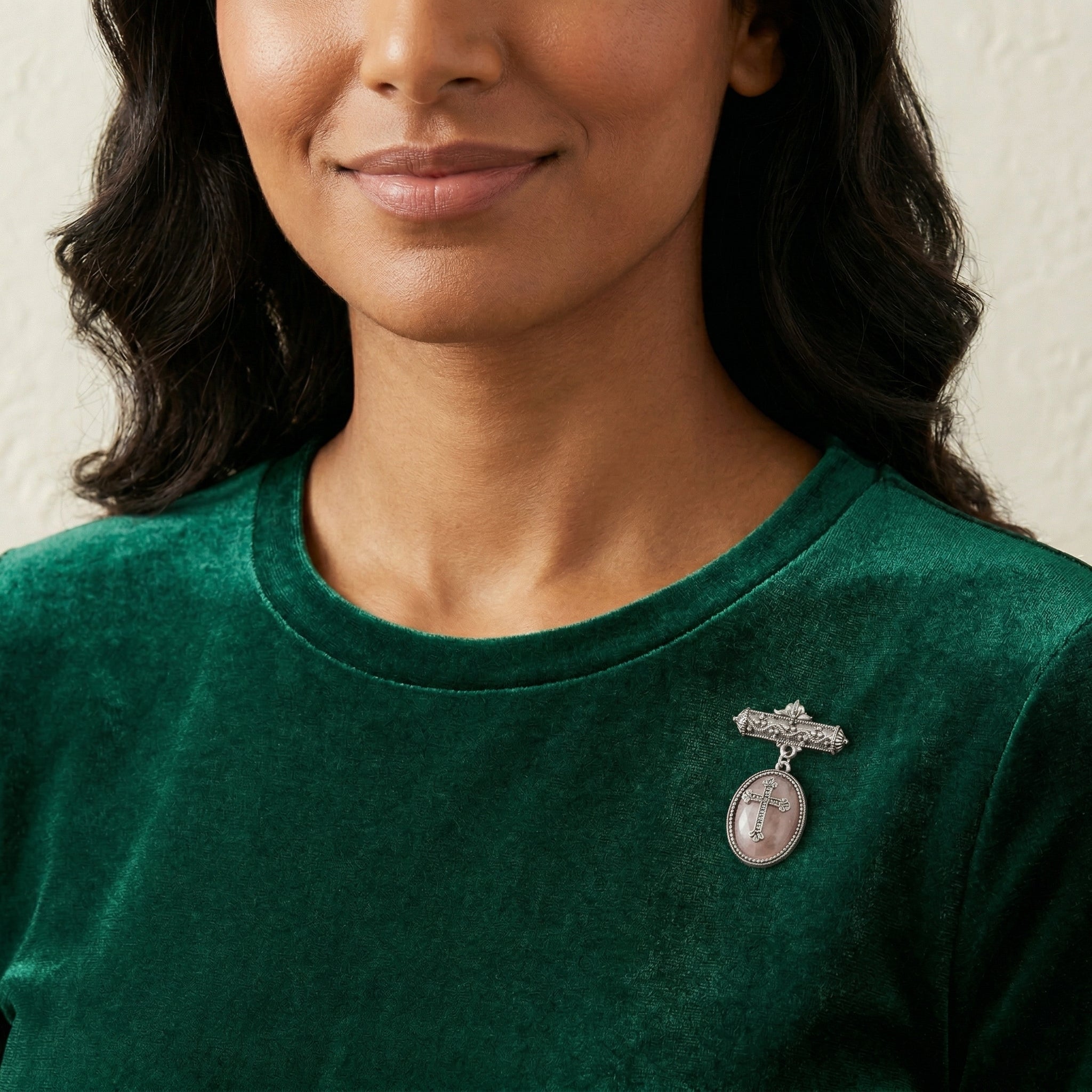 Woman wearing a green shirt with a gemstone cross brooch on a neutral background