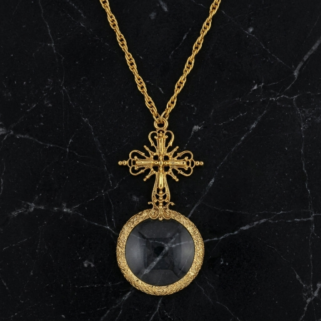 Gold necklace with a cross design and magnifying glass pendant on a black marble background