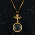 Gold necklace with a cross design and magnifying glass pendant on a black marble background