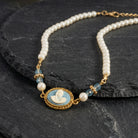 Aqua & Ivory Mother And Child Cameo Faux Pearl Strand Necklace resting on black stone surface