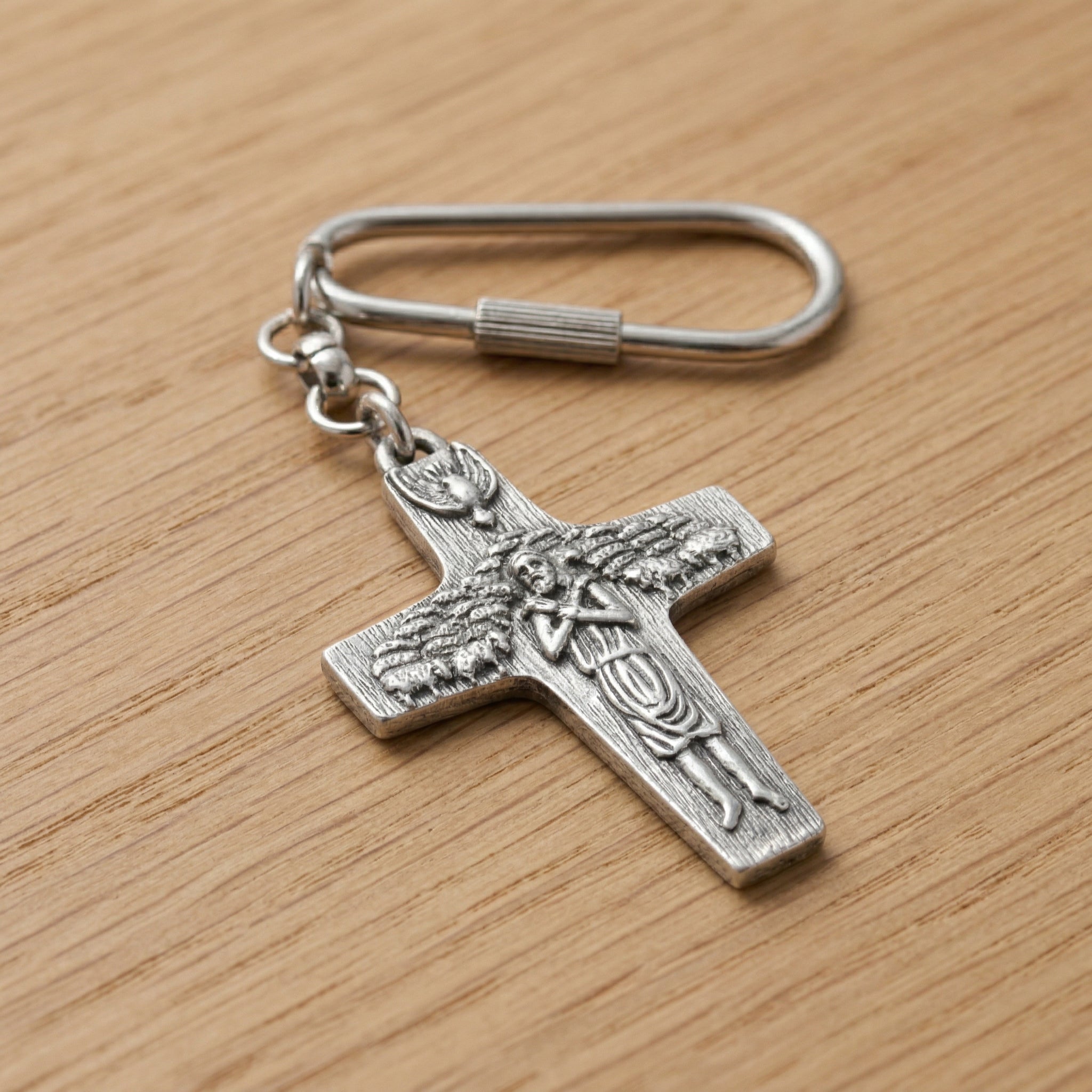 Silver cross keychain with angel design on a wooden surface
