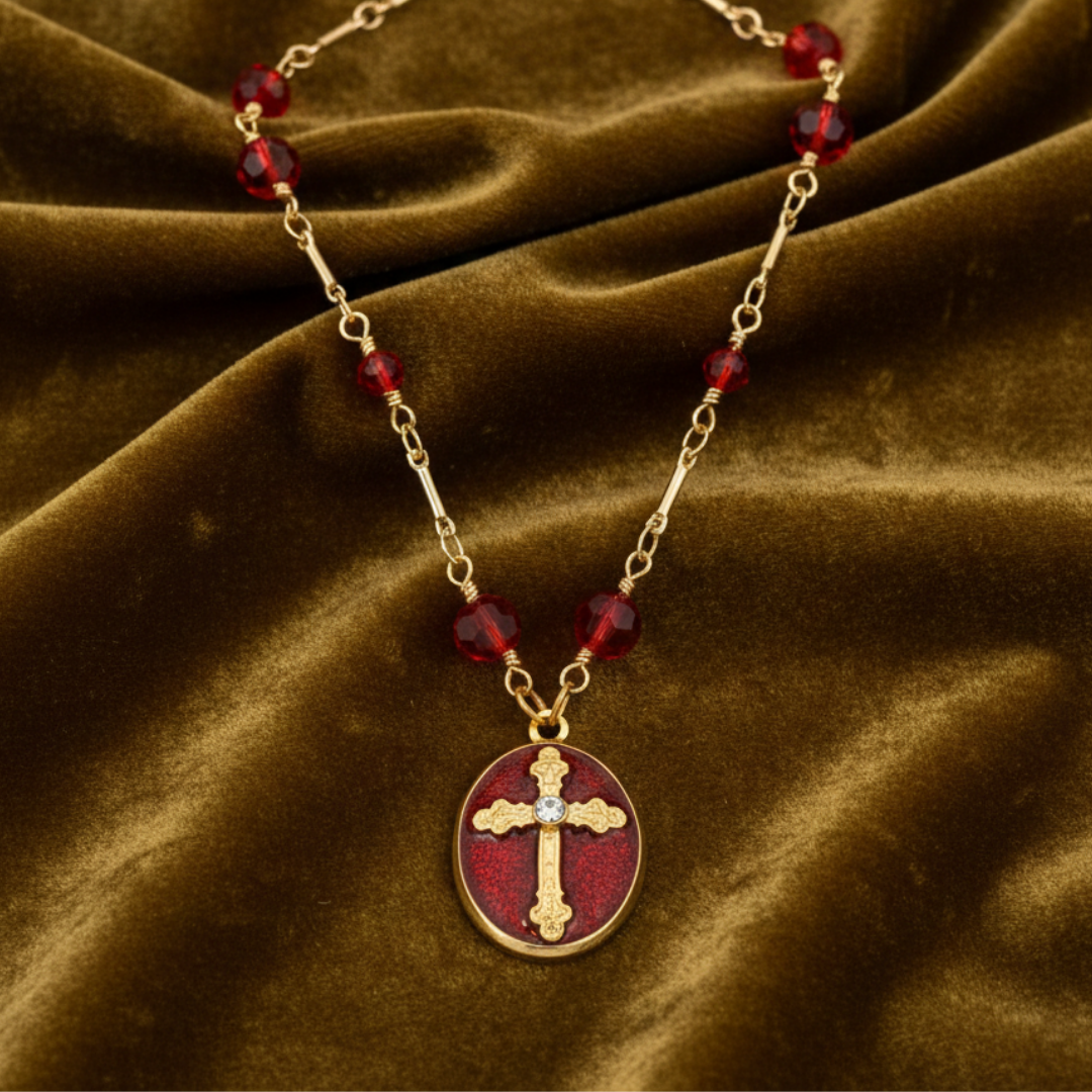 Necklace with red beads and a gold cross pendant on a brown fabric background.