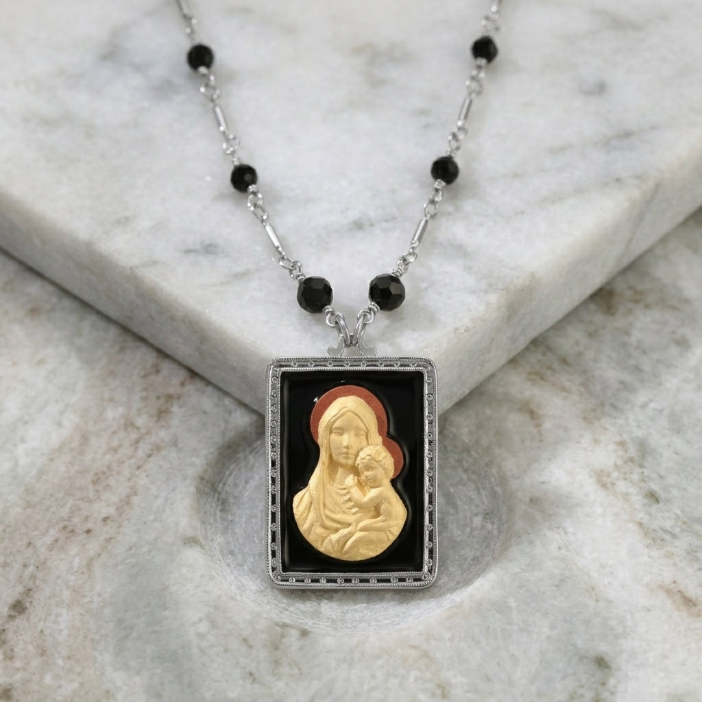 Black beaded, silver chain Madonna and Child pendant necklace on a marble surface. 
