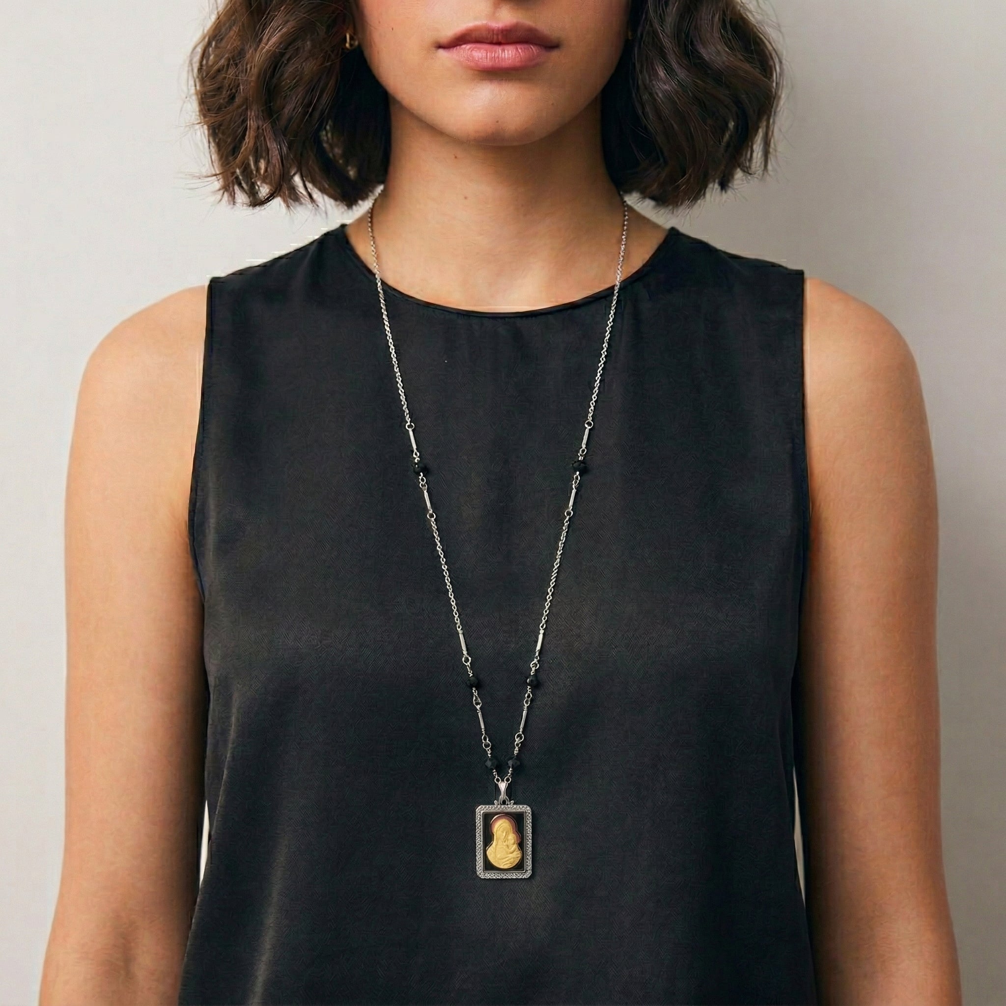 Person wearing a black sleeveless top with a long black beaded Madonna and Child pendant necklace.