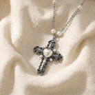 Silver cross necklace with faux pearl heart pendant and pearls on a beige fabric background
