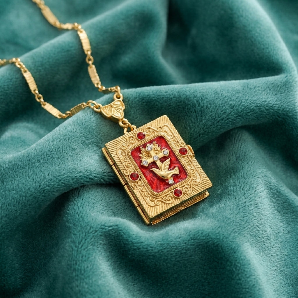 Gold necklace with a book-shaped Divine Grace cross and dove with red crystals on a teal fabric background