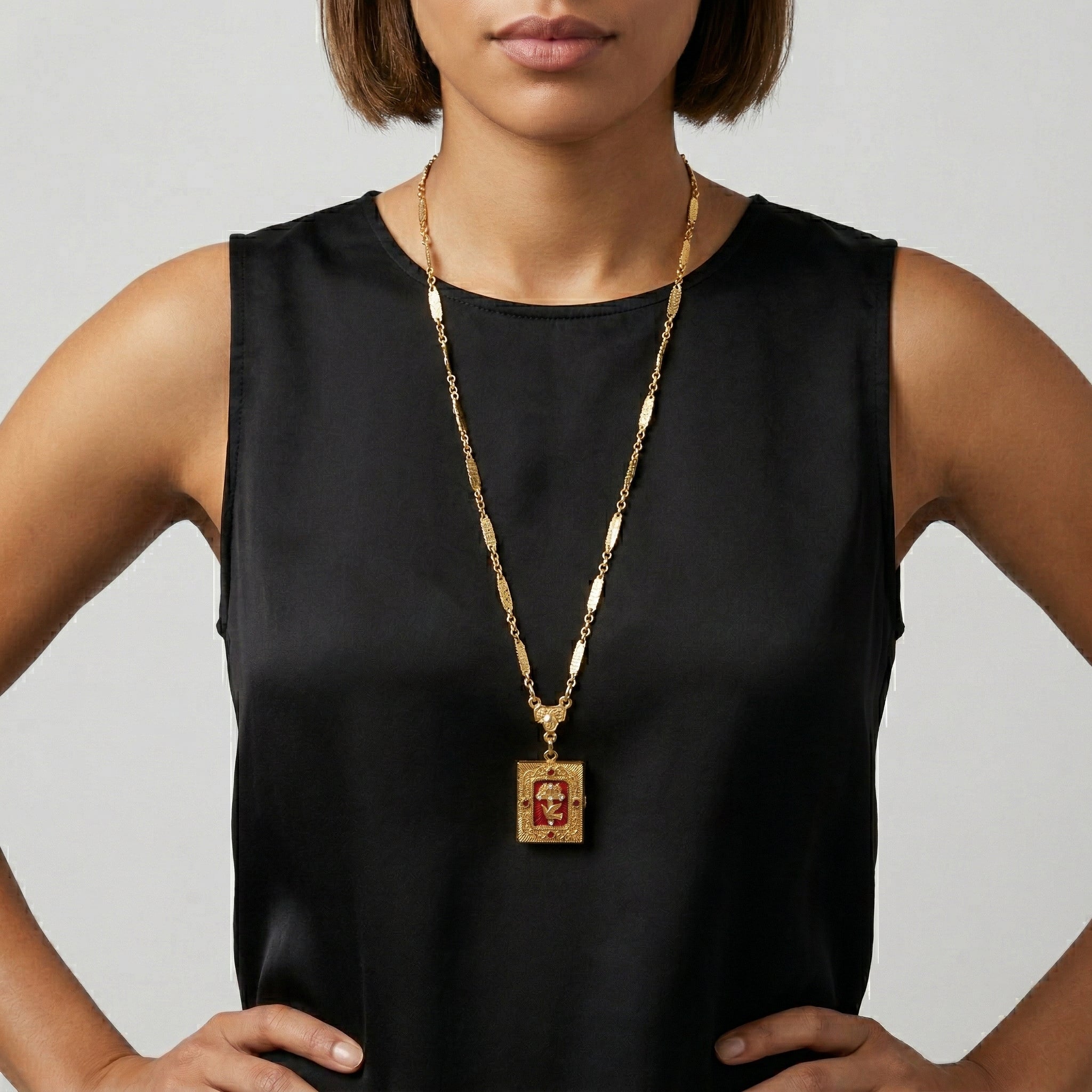 Woman wearing a black sleeveless top with a gold locket necklace featuring Divine Grace design and red crystals.