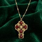 Gold necklace with a red crystal cross pendant on a green fabric background