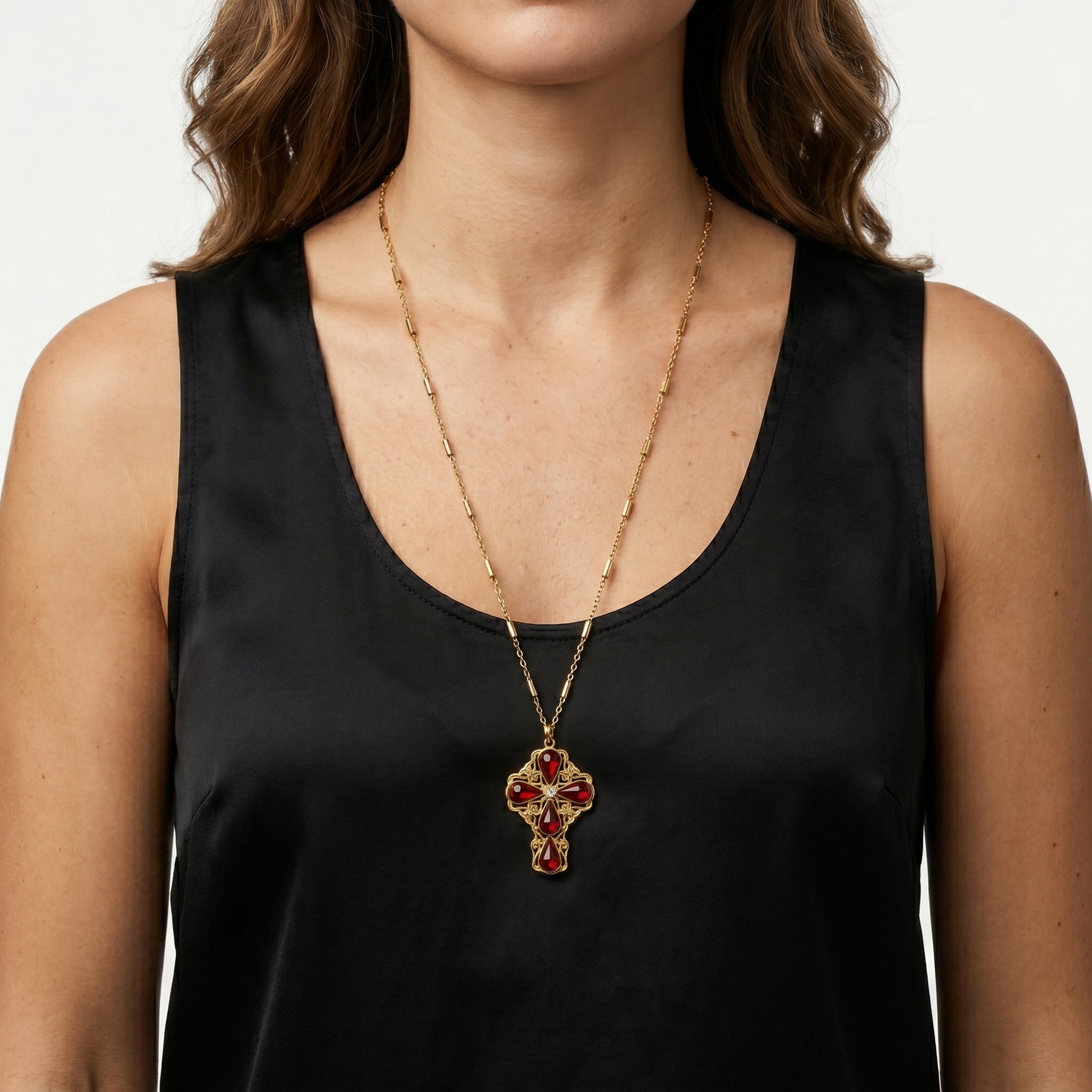 Woman wearing a gold tone tube link chain that has a cross pendant and red crystal accents