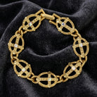 Gold bracelet with intricate design and AB crystals on a dark fabric background