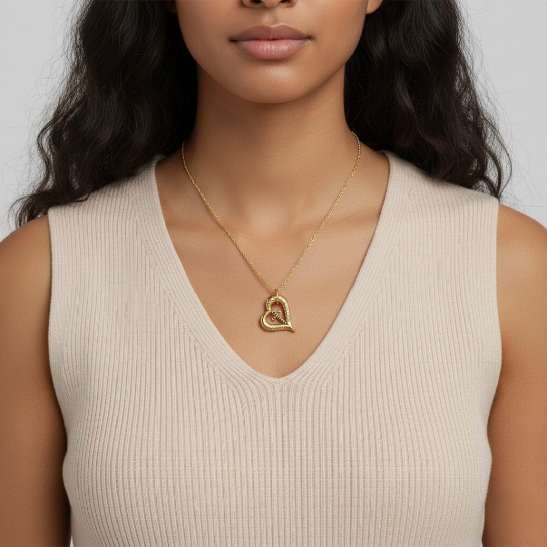 Woman wearing a gold heart-shaped necklace against a neutral background