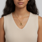 Woman wearing a gold heart-shaped necklace against a neutral background