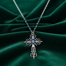 Silver cross necklace with blue stones on a green fabric background.