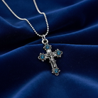 Silver cross necklace with blue stones on a blue fabric background