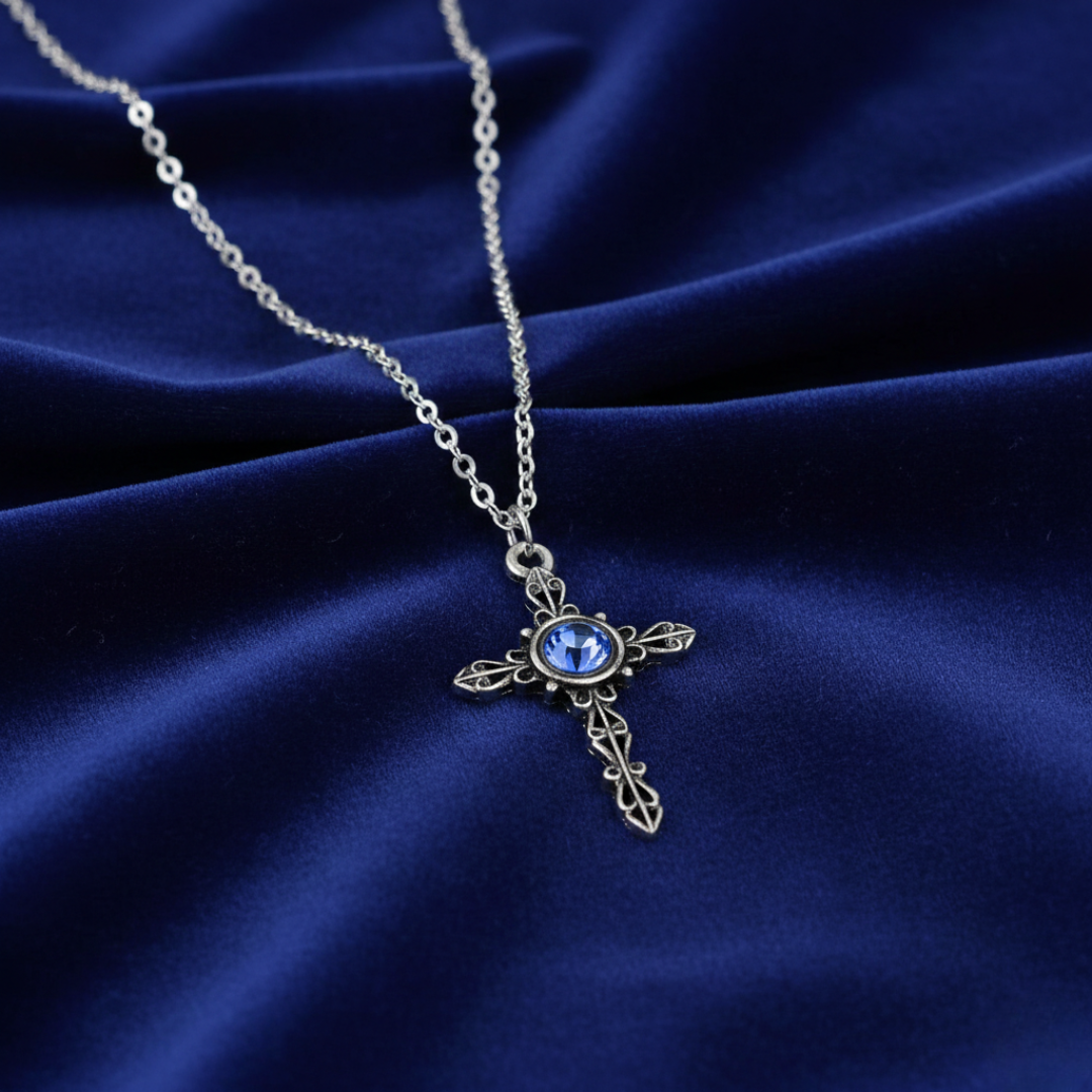 Silver cross necklace with a blue gemstone on a blue fabric background
