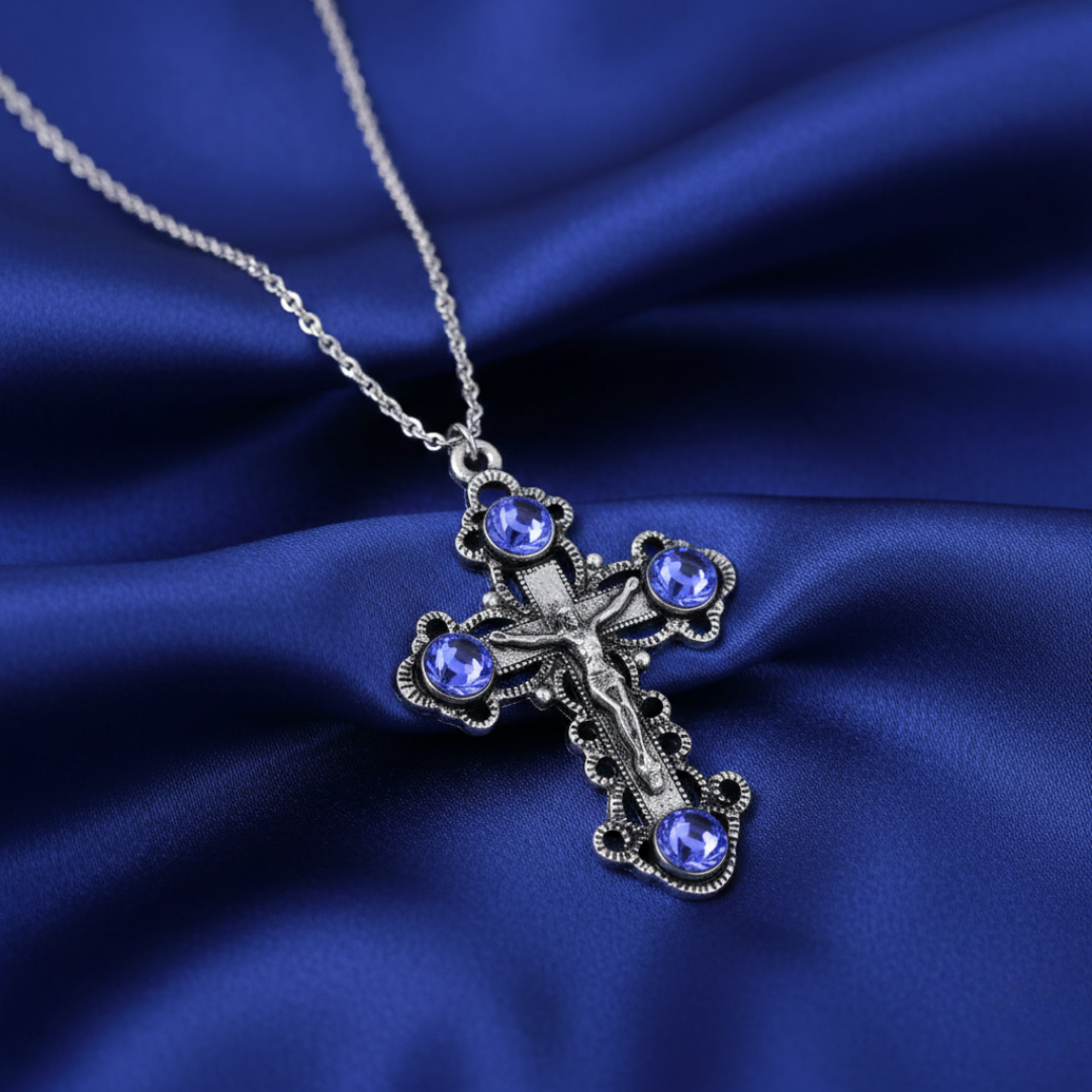 Silver cross necklace with blue gemstones on a blue satin background