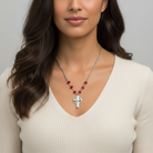 Woman wearing a necklace with a silver pendant and red beads against a neutral background