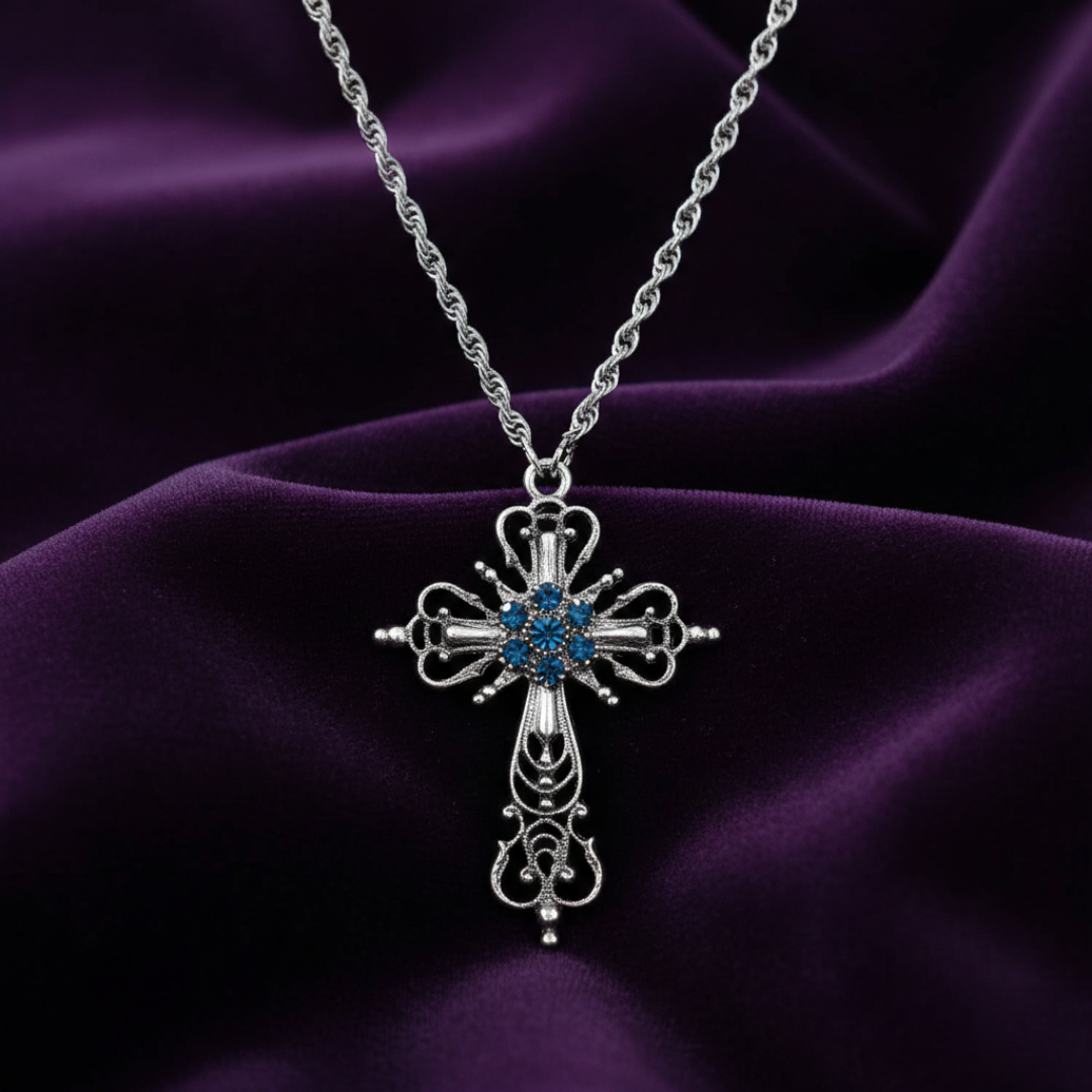 Silver cross necklace with blue stones on a purple fabric background