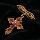 Decorative cross brooch with red gemstones and gold tone detailing on a black background