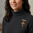 Woman wearing a dark gray turtleneck sweater with a decorative cross brooch.