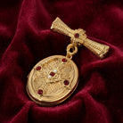 Gold cross brooch locket in closed position with red gemstones on a red fabric background