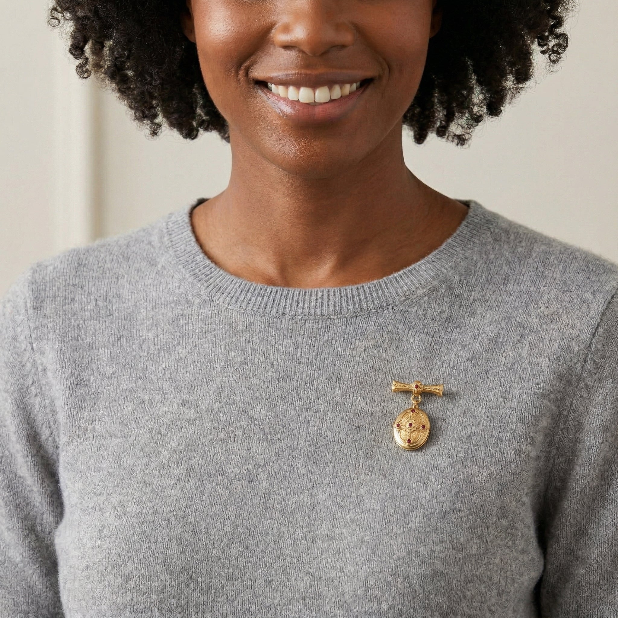 Woman wearing a gray sweater with a gold brooch locket on a neutral background