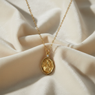 Gold necklace with a pendant of Mary praying on a beige fabric background