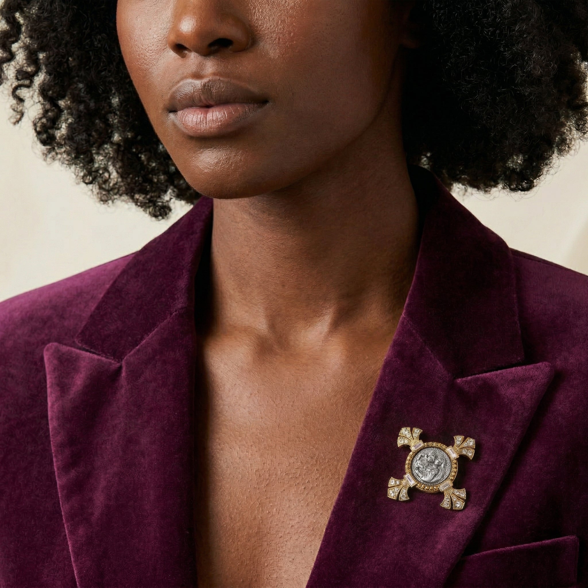Woman wearing a purple blazer with a decorative religious brooch against a neutral background