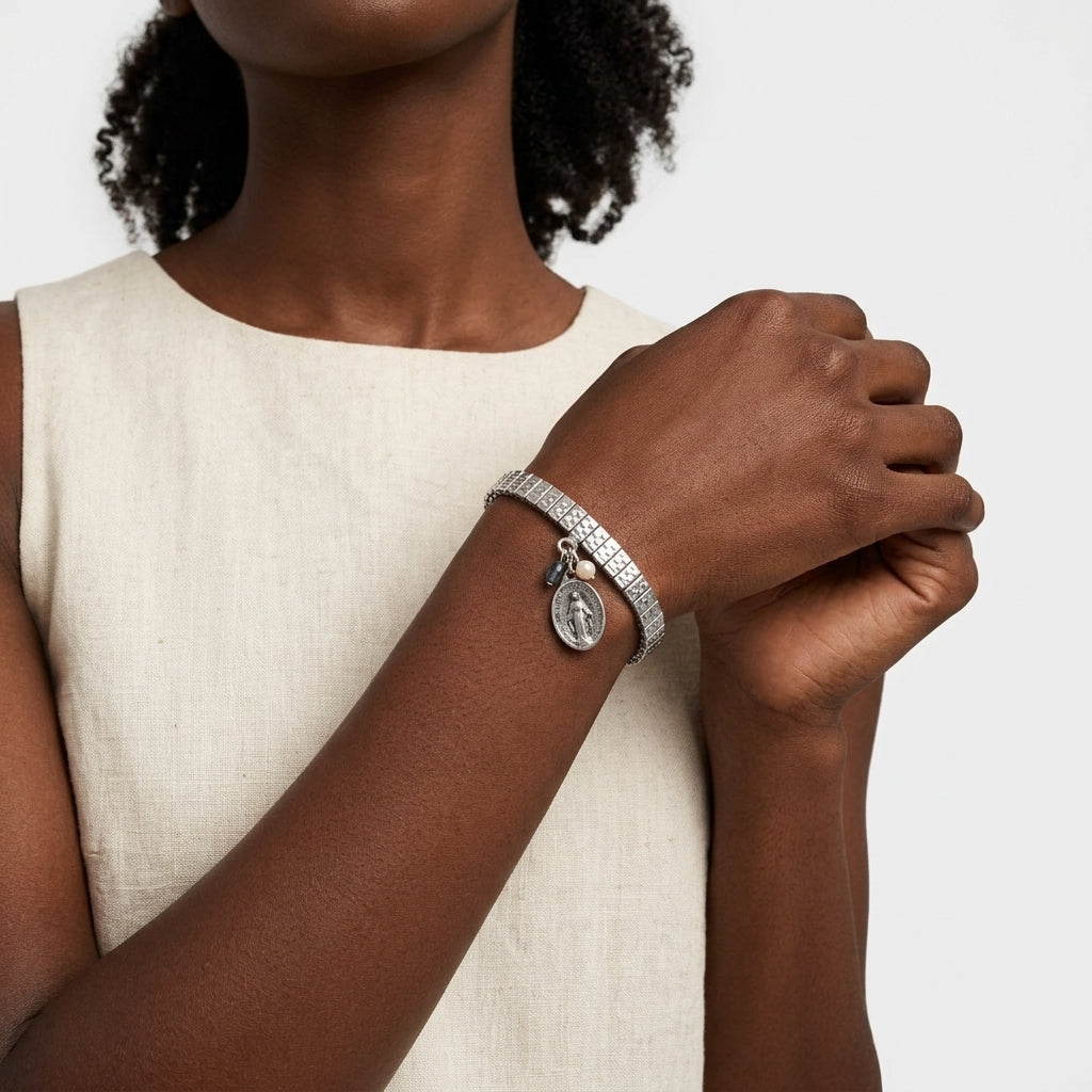 Person wearing a silver bracelet with a Jesus charm and pearl on a neutral background
