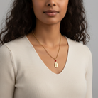 Woman wearing a gold necklace with a pendant against a neutral background