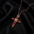Siam red crystal cross necklace and beads on gold tone metal resting on top of black fabric