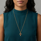 Woman wearing a gold necklace with a cross pendant and red crystal on a gray background