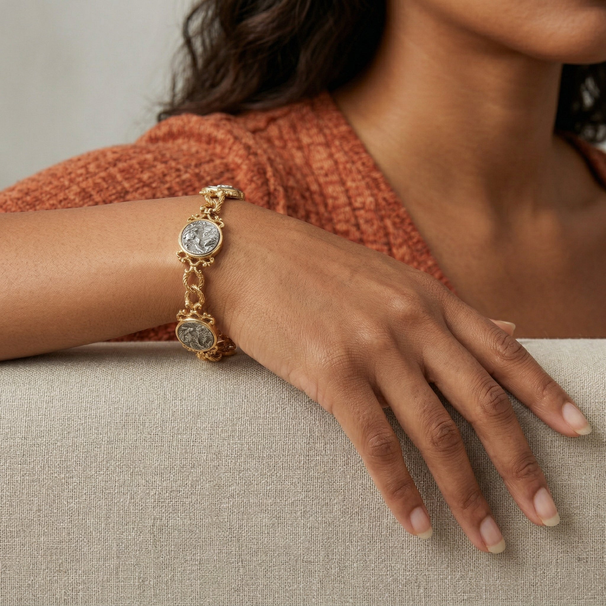 Close-up of a hand wearing a gold bracelet with silver tone angel playing the trumpet designs on a neutral background
