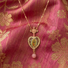 Gold necklace with a heart-shaped pendant featuring a religious figure on a pink fabric background