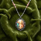 Holy Family pendant necklace with raspberry beads resting on a dark green fabric surface. 