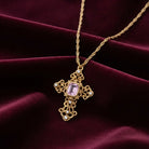 Gold cross necklace with a pink crystal and AB crystal accents on a maroon fabric background