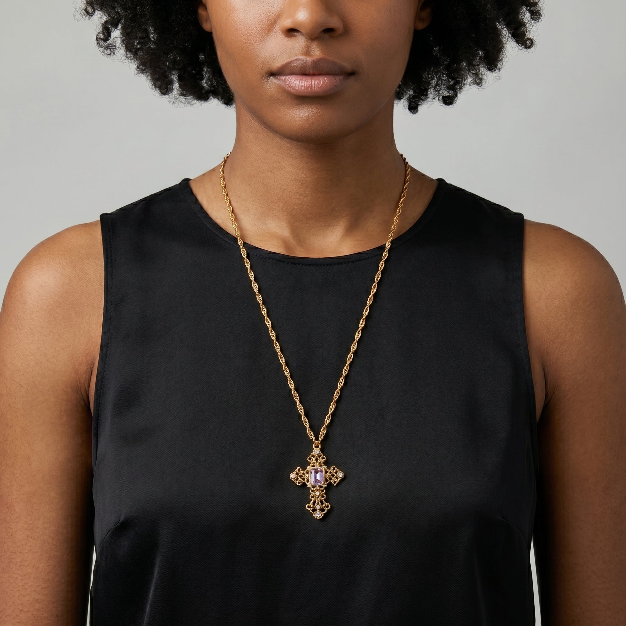 Woman wearing a gold tone necklace with cross pendant that has a light purple amethyst crystal and AB crystal accents.