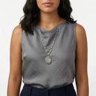 Woman wearing a gray sleeveless top with a Virgin Mary pendant locket necklace on a white background