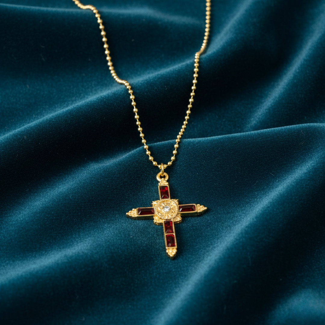 Gold cross necklace with red accents on a blue velvet background