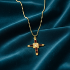 Gold cross necklace with red accents on a blue velvet background