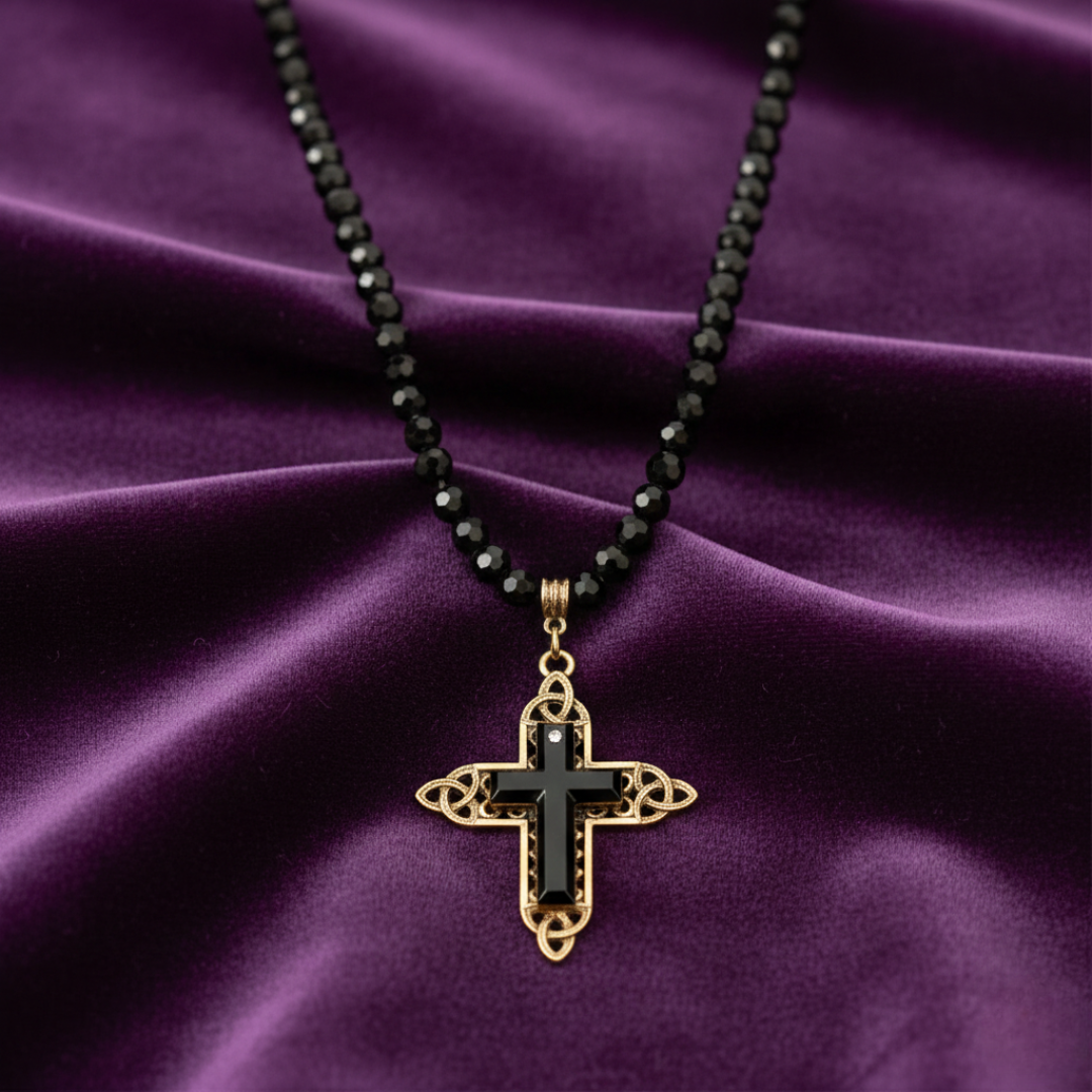 Necklace with black beaded chain and gold cross pendant on purple fabric.