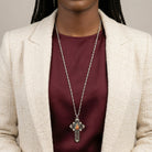 Person wearing a silver cross necklace with a Mother Mary and Child pendant on a neutral background