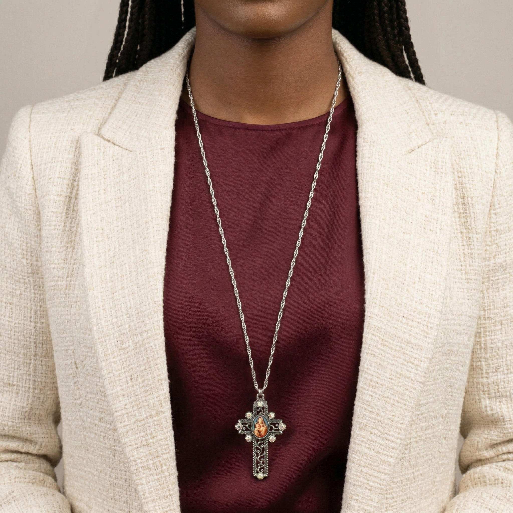 Person wearing a silver cross necklace with a Mother Mary and Child pendant on a neutral background