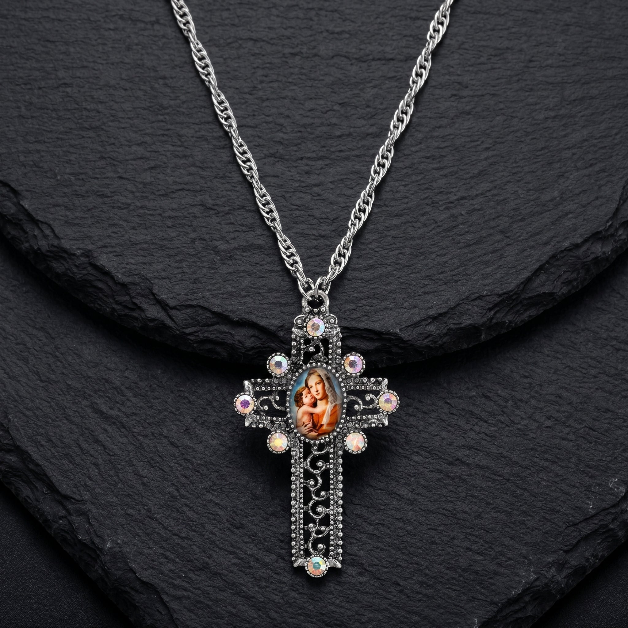 Silver cross necklace with a Mother Mary and Child pendant on a dark stone background