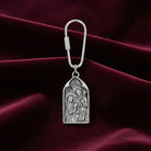 Silver keychain with religious design on a maroon fabric background