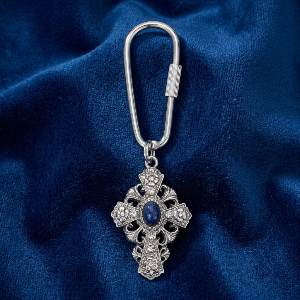 Silver cross-shaped keychain with a blue gemstone on a blue fabric background