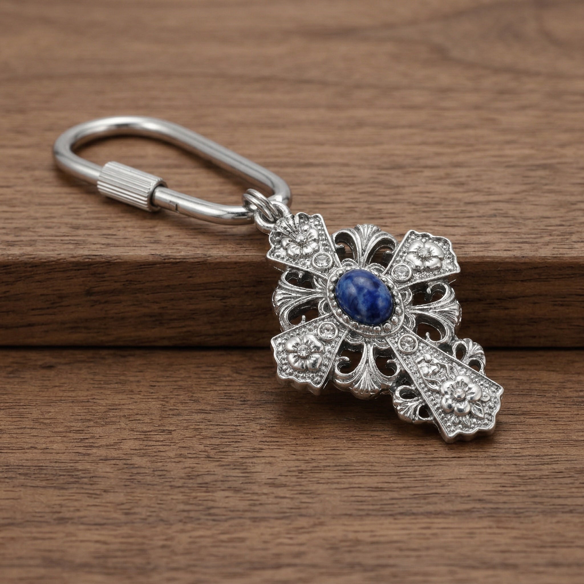 Silver cross design keychain with decorative and blue gemstone on a wooden surface