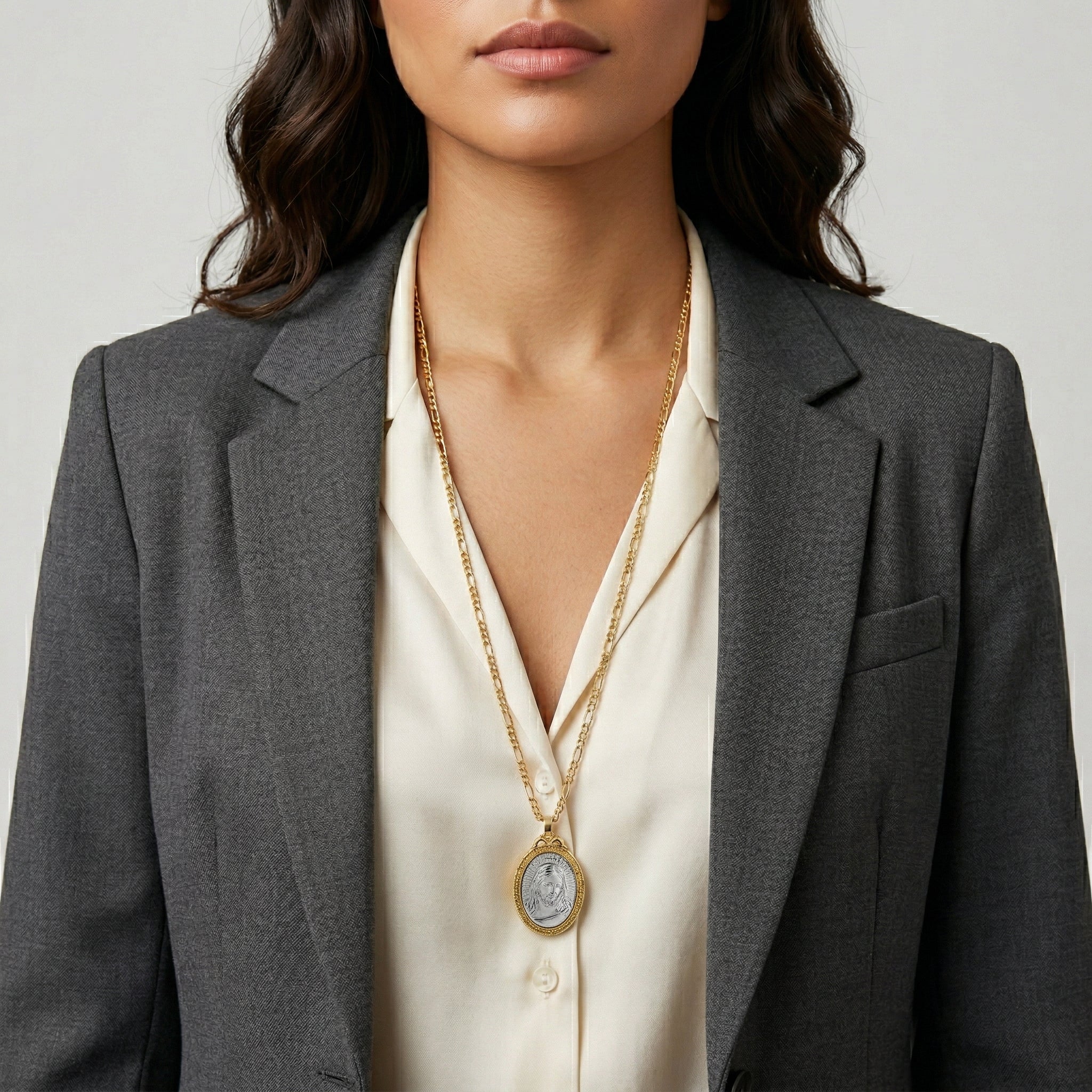 Woman wearing a gold necklace with a religious Jesus pendant against a neutral background