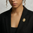 Woman in a black blazer wearing an all-Gold Jesus brooch