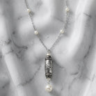 Religious necklace with bible snippets and white faux pearls and an ornate pendant on a marble surface